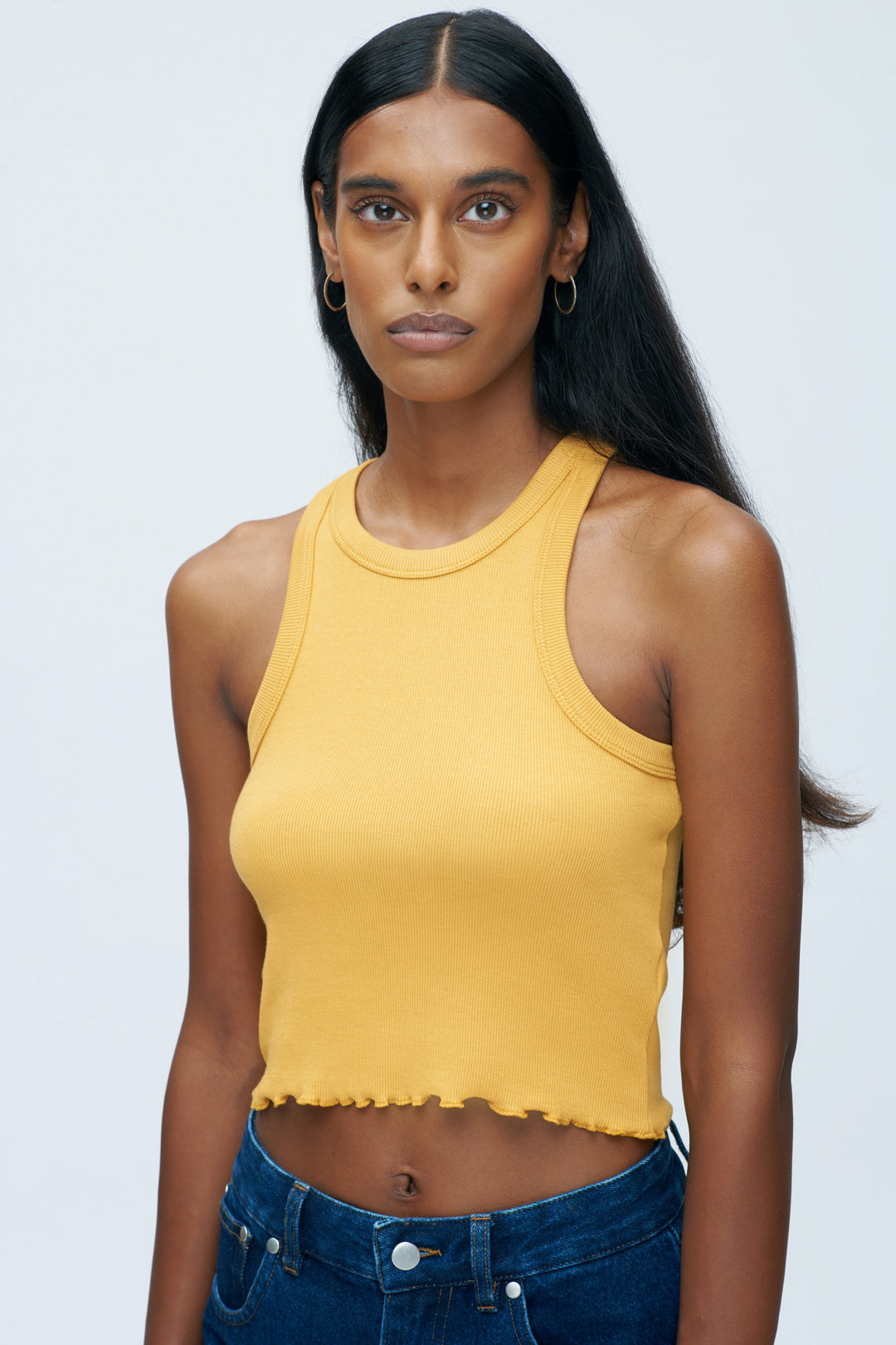 A lady wears a mustard colored fitted crop top by fair trade fashion brand KOTN.